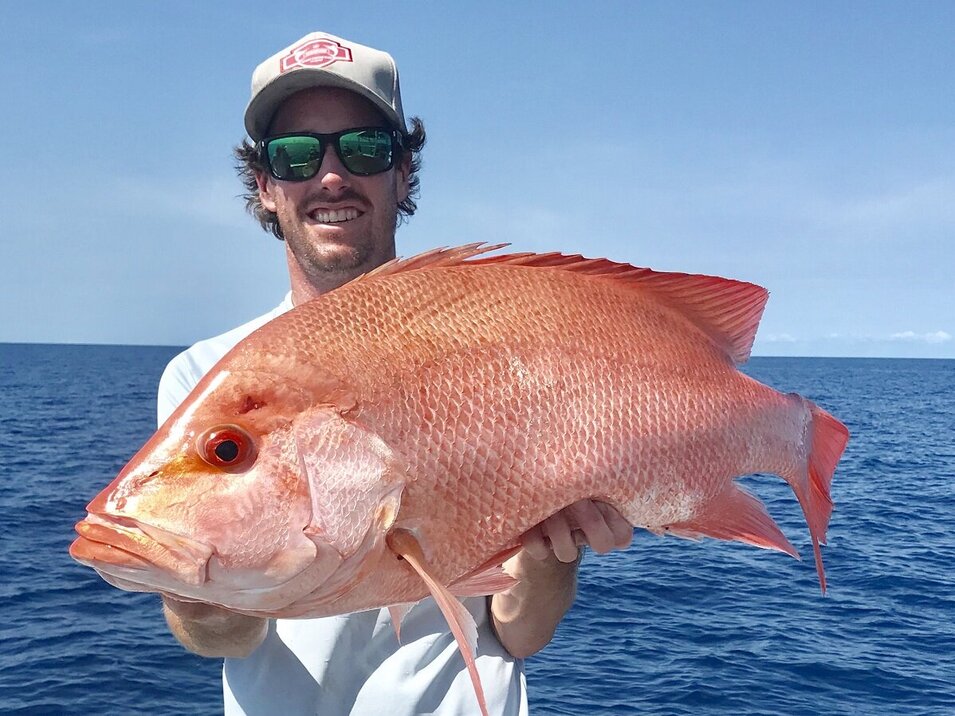 male angler wearing white cap holding a great barrier reef fish