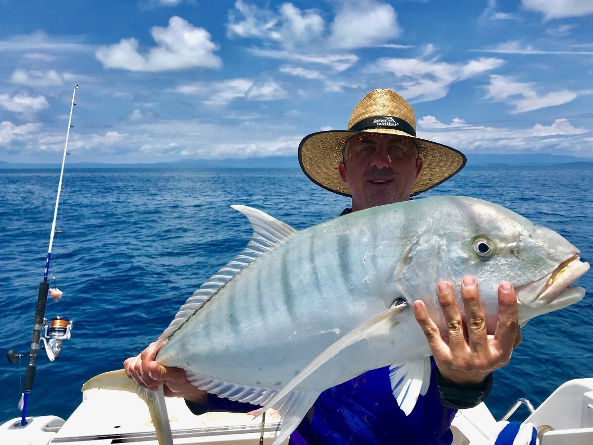 Man with sun hat holding a trevally fish